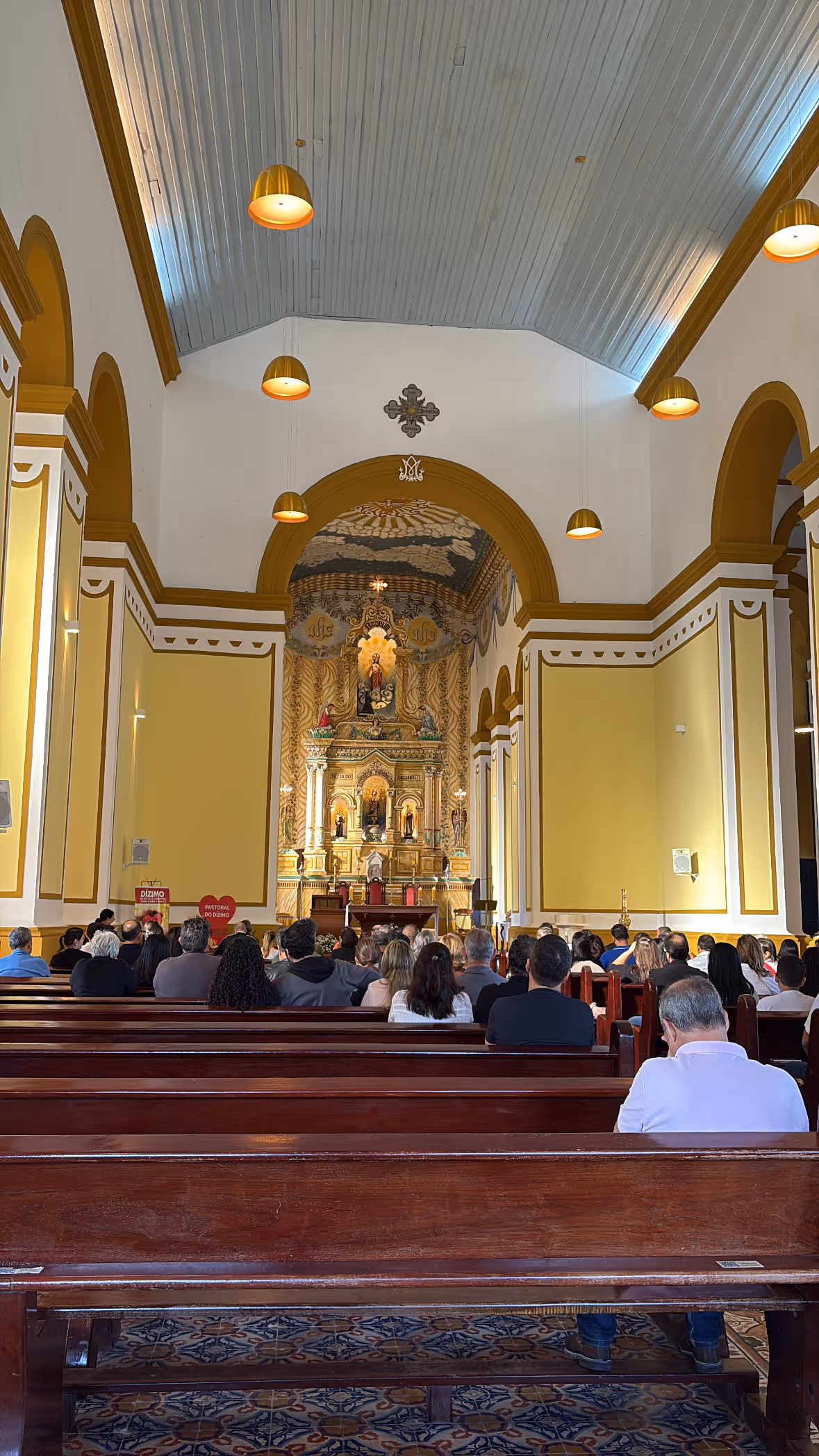 Inside a church during Mass, gold altar at the end of the nave